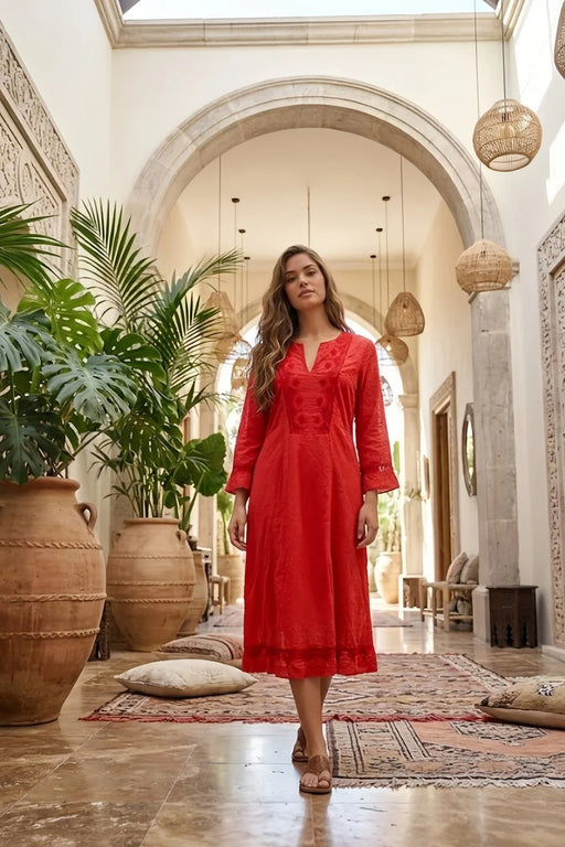 Woman in a red dress standing in a stylish interior setting with plants and decor.