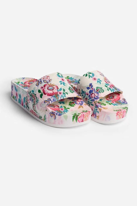 A pair of platform slide sandals with a vibrant multicolor floral print on a white base, shown against a plain light gray background.