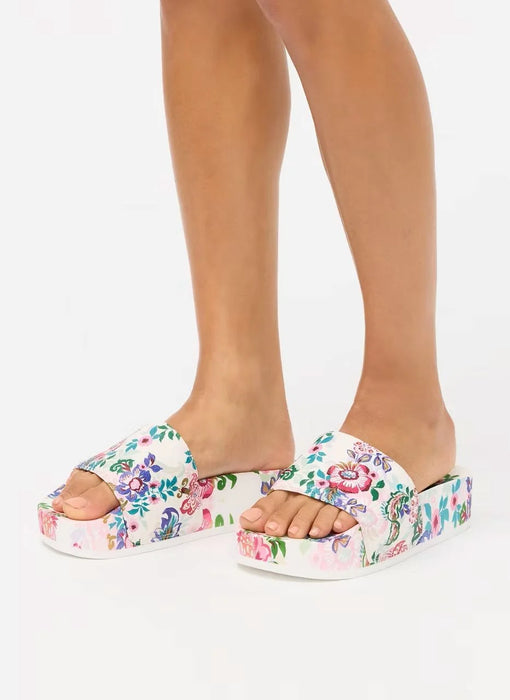 A pair of platform slide sandals with a colorful floral print on a white base, shown on a model's feet against a plain white background.