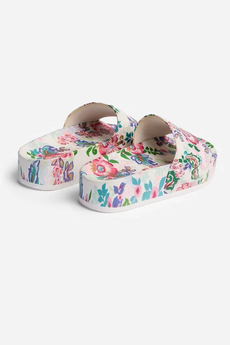 A pair of platform slide sandals featuring a vibrant multicolor floral print on a white base, shown against a light gray studio background.