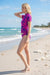 Woman in a pink swimsuit standing on a beach with ocean waves in the background