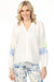 Woman wearing white button front v-neck blouse with floral embroidered raglan sleeves from Charlie B