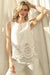 Woman wearing a sleeveless cream top with eyelet embroidered scallopedhem details from Charlie B