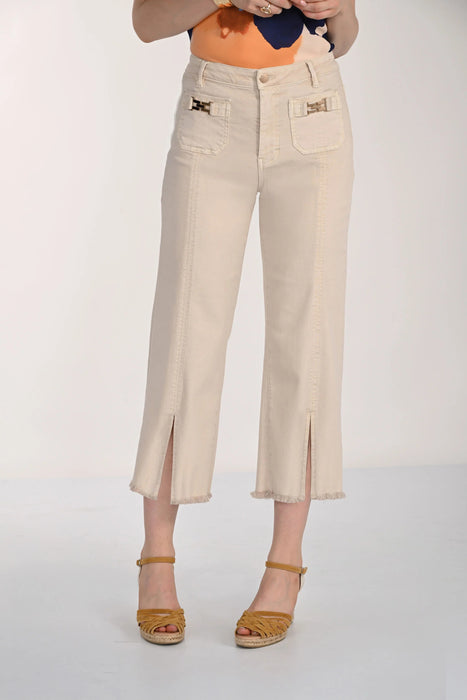 A model is wearing a pair of cropped, wide-leg denim pants in a light beige color, styled with mustard yellow espadrille sandals and an orange top against a plain white studio background.