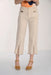 A model is wearing a pair of cropped, wide-leg denim pants in a light beige color, styled with mustard yellow espadrille sandals and an orange top against a plain white studio background.