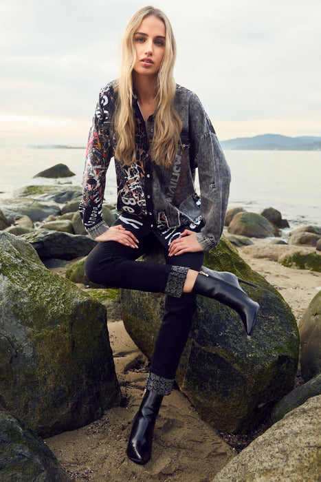 Woman sitting on rocks by a body of water wearing a patterned top and dark pants.