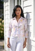A woman stands outdoors against a white house wall wearing a light pink button-up jacket with a soft floral print from Frank Lyman
