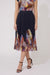 A model wearing a pleated midi skirt with a dark navy base and a colorful abstract floral print at the waist and hem, paired with black strappy high-heeled sandals against a plain light gray studio background.