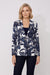 A woman modeling a navy blue and white tropical leaf print blazer over a black top and dark jeans, standing against a light gray studio background.