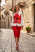 A woman walking down a cobblestone street wearing a white blazer with a large red hibiscus floral print on the front from Frank Lyman