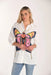 A woman modeling a white long-sleeve button-up shirt featuring a large, colorful butterfly graphic on the front, paired with light blue jeans against a plain white studio background.