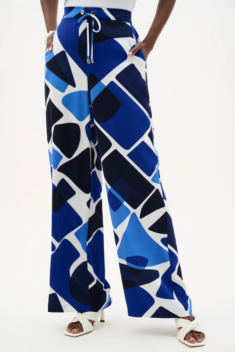 Woman wearing Joseph Ribkoff geometric print wide leg pull-on pants 262155, featuring a bold pattern, flowy silhouette, elastic waistband, and a flattering modern fit.
