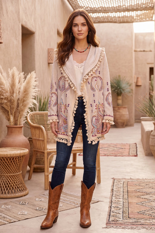 Woman wearing a beige open front hoodie cardigan with paisley embroidery and tassel trim along the edges from Johnny Was