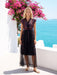 A woman modeling a black midi dress with colorful bohemian embroidery and sheer tulle hem, standing outdoors on a white terrace with a blue sea and pink bougainvillea flowers in the background.