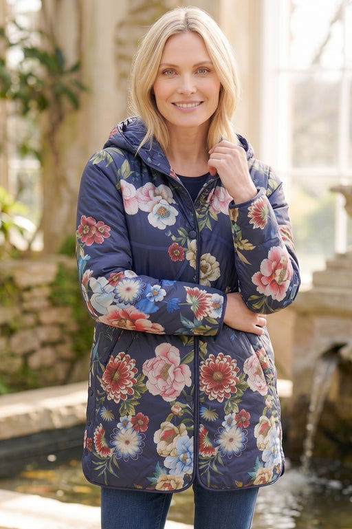 Woman wearing a navy quilted puffer jacket with colorful florals and hood from Johnny Was