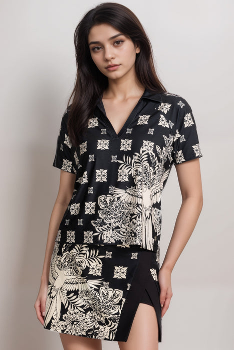 Woman wearing a black, lightweight, boxy polo tee with contrasting bird and floral pattern