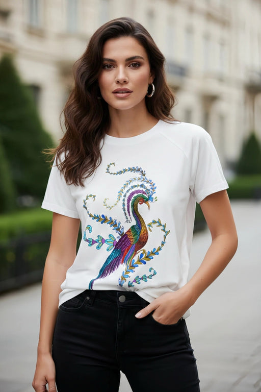 Woman wearing a white crew neck raglan t-shirt with a colorful peacock graphic design from Johnny Was