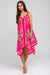 Woman wearing a bright pink dress with floral pattern and handkerchief hem from Johnny Was