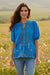 Woman wearing a blue embroidered v-neck blouse with button front and puff sleeves from Johnny Was