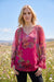 Woman wearing a pink printed mesh top with lace trim and split v-neck with tie from Johnny Was