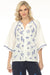 Woman wearing a white top with blue embroideries and button front closure from Johnny Was