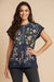 Woman wearing a navy embroidered blouse with floral patterns, henley and short sleeves from Johnny Was
