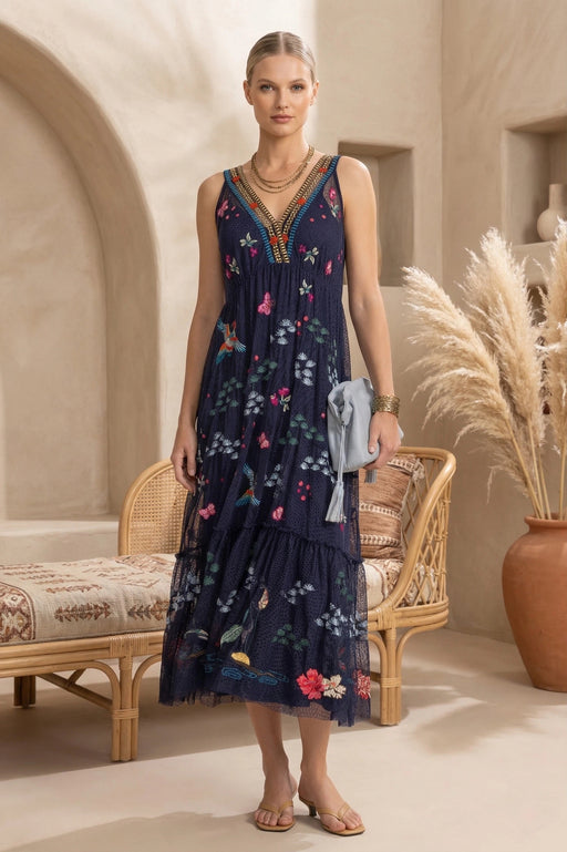 Woman wearing a blue v-neck sleeveless midi dress with floral embroidery and tiered hem from Johnny Was