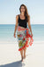 Woman walking on a beach wearing a colorful floral sarong with red tassels from Johnny Was