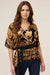 Woman wearing a gold and black patterned top with v-neck and elbow sleeves from Johnny Was