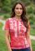 A woman wearing a short-sleeve collared top with a red and white floral pattern, paired with blue jeans, standing outdoors against a blurred green background.