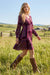 A woman wearing a long-sleeve purple and magenta paisley V-neck dress from Johnny Was