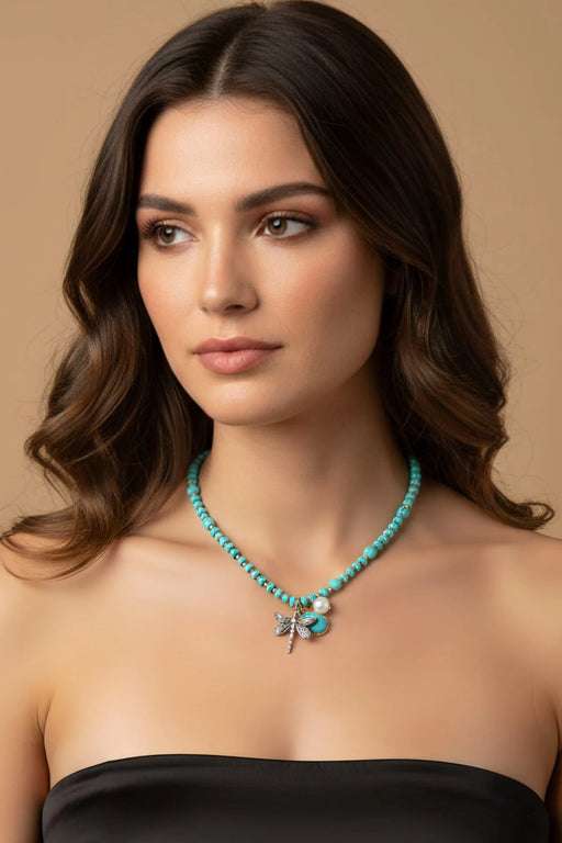Woman wearing a turquoise and gold beaded necklace with silver dragonfly, teardrop, and pearl charm from Johnny Was