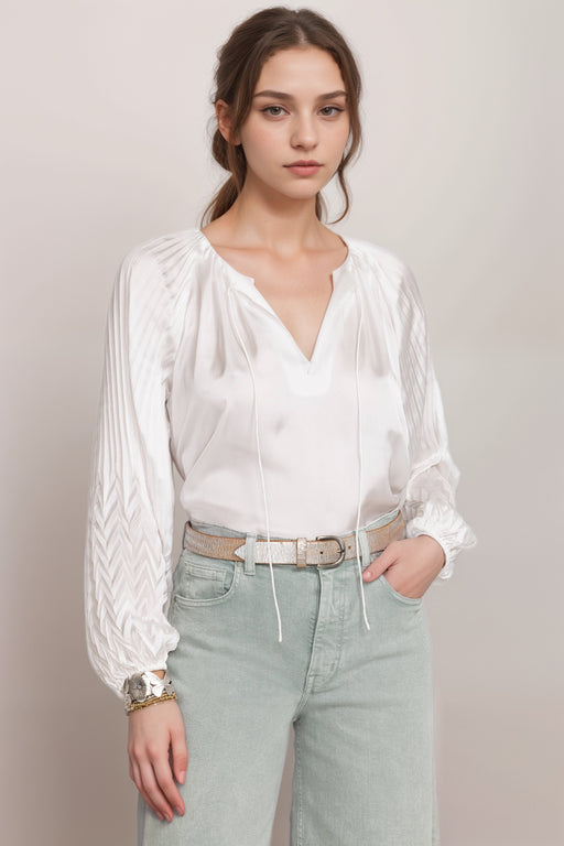 Woman wearing a white shiny blouse with pleated puff sleeves and split v-neck with tie from Johnny Was