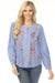 Woman wearing a blue striped blouse with colorful embroideries and henley neckline from Johnny Was