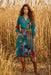 Woman wearing a vibrant turquoise floral printed midi dress with v-neck and side pockets from Johnny Was