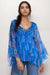 Woman wearing a blue sheer floral silk blouse with ruffles and tie neck
