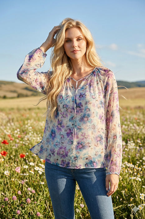 Woman wearing a semi-sheer floral printed long sleeve blouse with split neck tie from Johnny Was