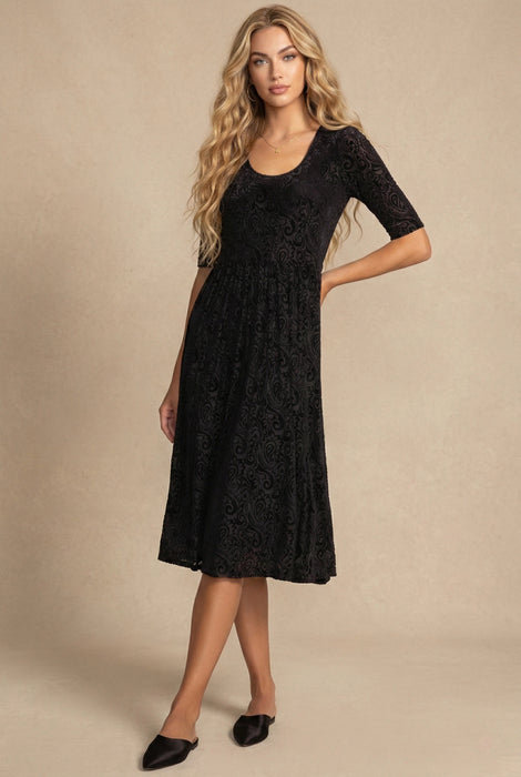 Woman wearing a black midi fit and flare dress with paisley pattern and scoop neck from Johnny Was