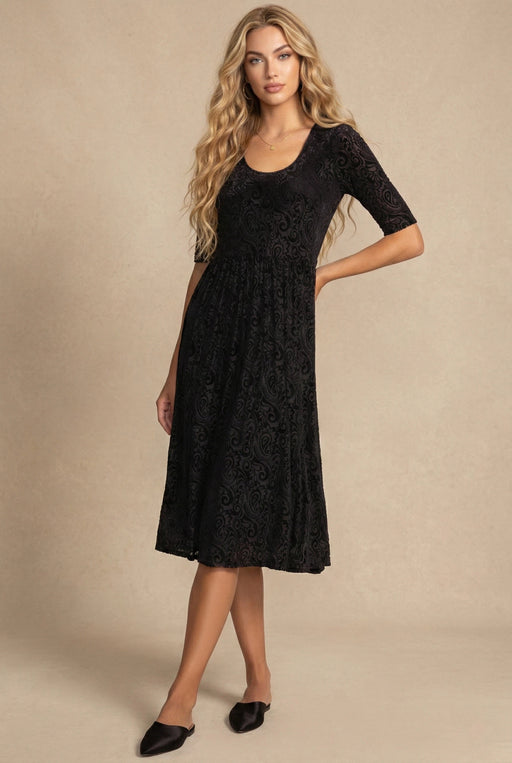 Woman wearing a black midi fit and flare dress with paisley pattern and scoop neck from Johnny Was