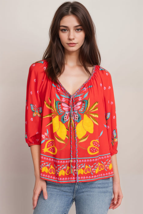Woman wearing a red blouse with butterfly patterns and v-neck braid tie from Johnny Was