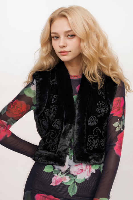 Woman wearing a black embroidered velvet vest with faux fur trim on the edges