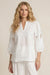 Woman wearing a white embroidered blouse with split v-neck and puff sleeves from Johnny Was