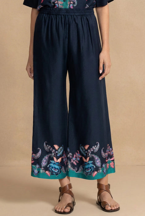 Woman wearing a navy blue cropped wide leg pants with floral print at the hem and pull on elastic waistband from Johnny Was