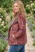 A woman wearing a long-sleeve quilted jacket with a multicolor paisley pattern in purple, orange, and brown, standing in a garden pathway.