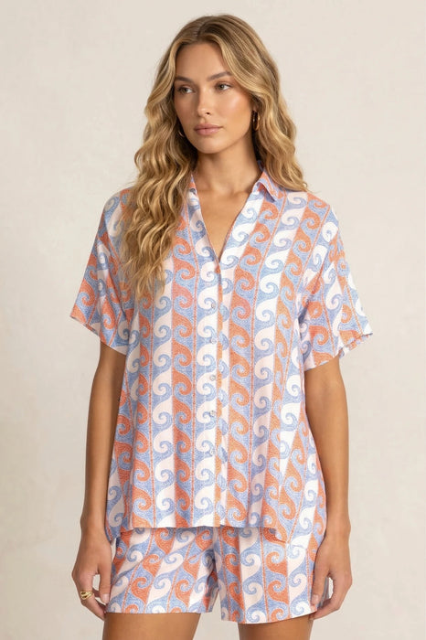 Woman wearing a short sleeve shirt with orange and blue waves pattern and button front from Johnny Was
