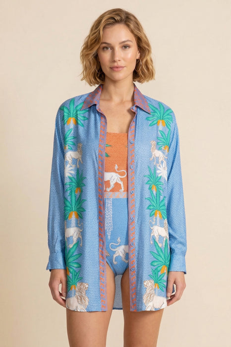 Woman wearing a blue lightweight button down shirt with colorful palm tree and lion prints from Johnny Was