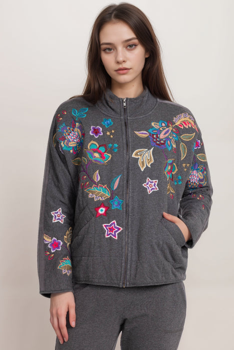 Woman wearing a gray jacket with colorful floral embroidery on a solid quilted background