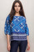 Woman wearing a blue linen blouse with tile-like pattern and fair isle hem