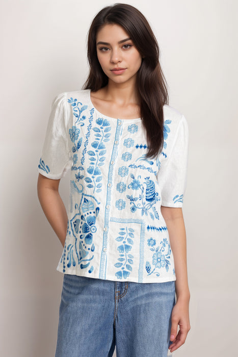 Woman wearing a white linen blouse with blue embroideries and button front from Johnny Was