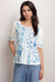 Woman wearing a white linen blouse with blue embroideries and button front from Johnny Was
